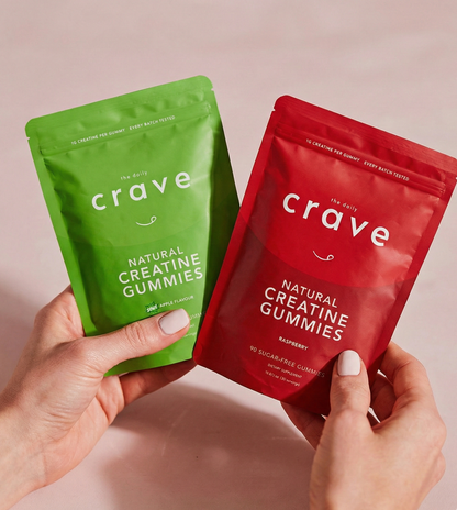 Two packages of 'crave' natural creatine gummies, one green and one red, held by hands against a light pink background.